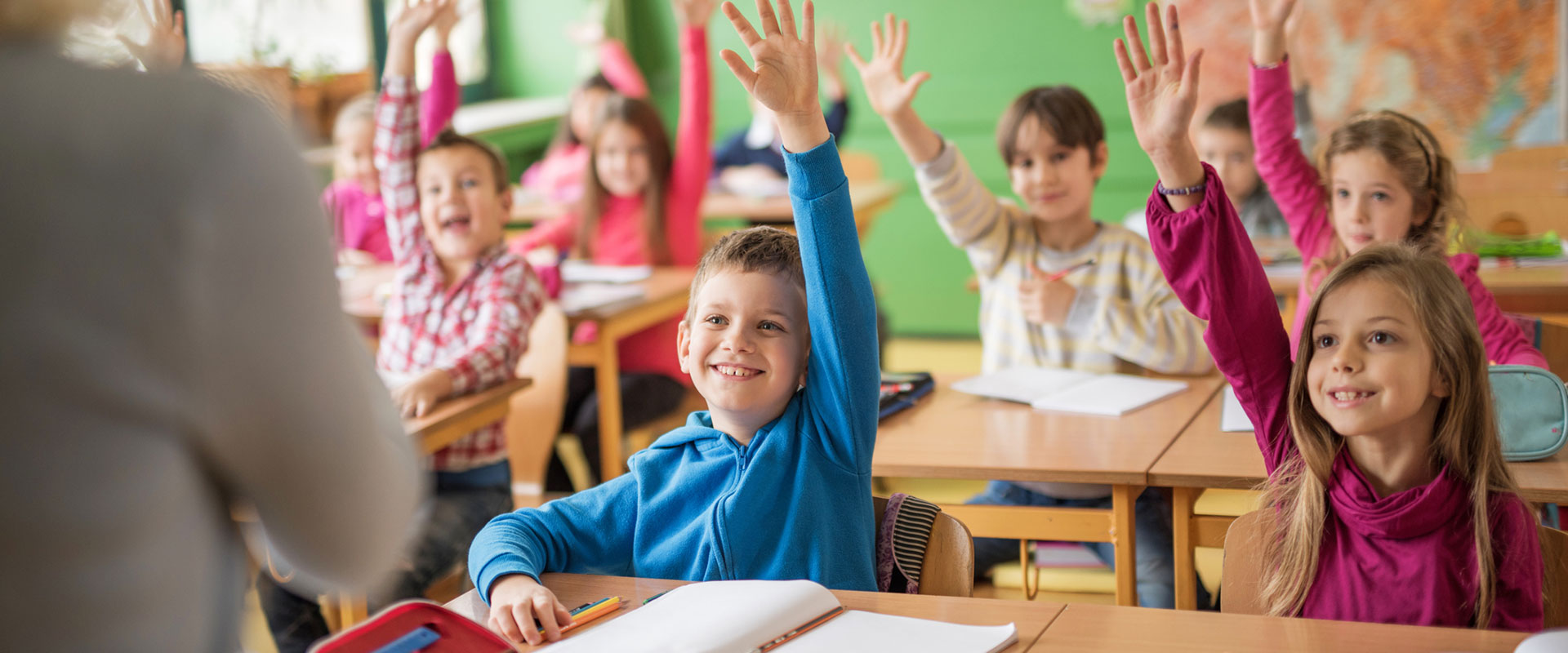Kinder in Österreichen sitzen in einer Schulklasse und zeigen auf